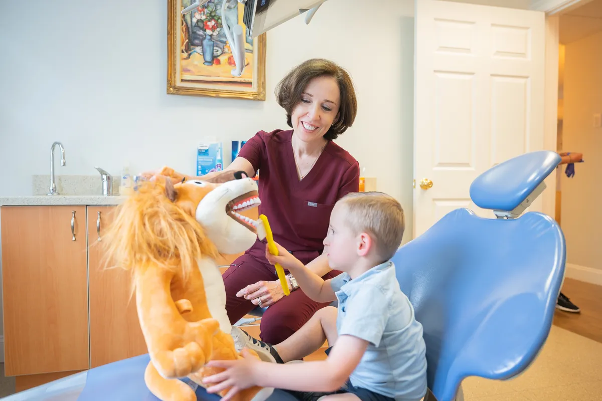 A dentist using a puppet to demonstrate toothbrushing to a child