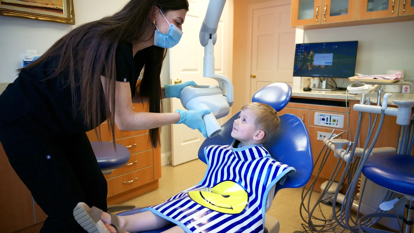 A dental team member positioning a digital X-ray for a smiling young patient