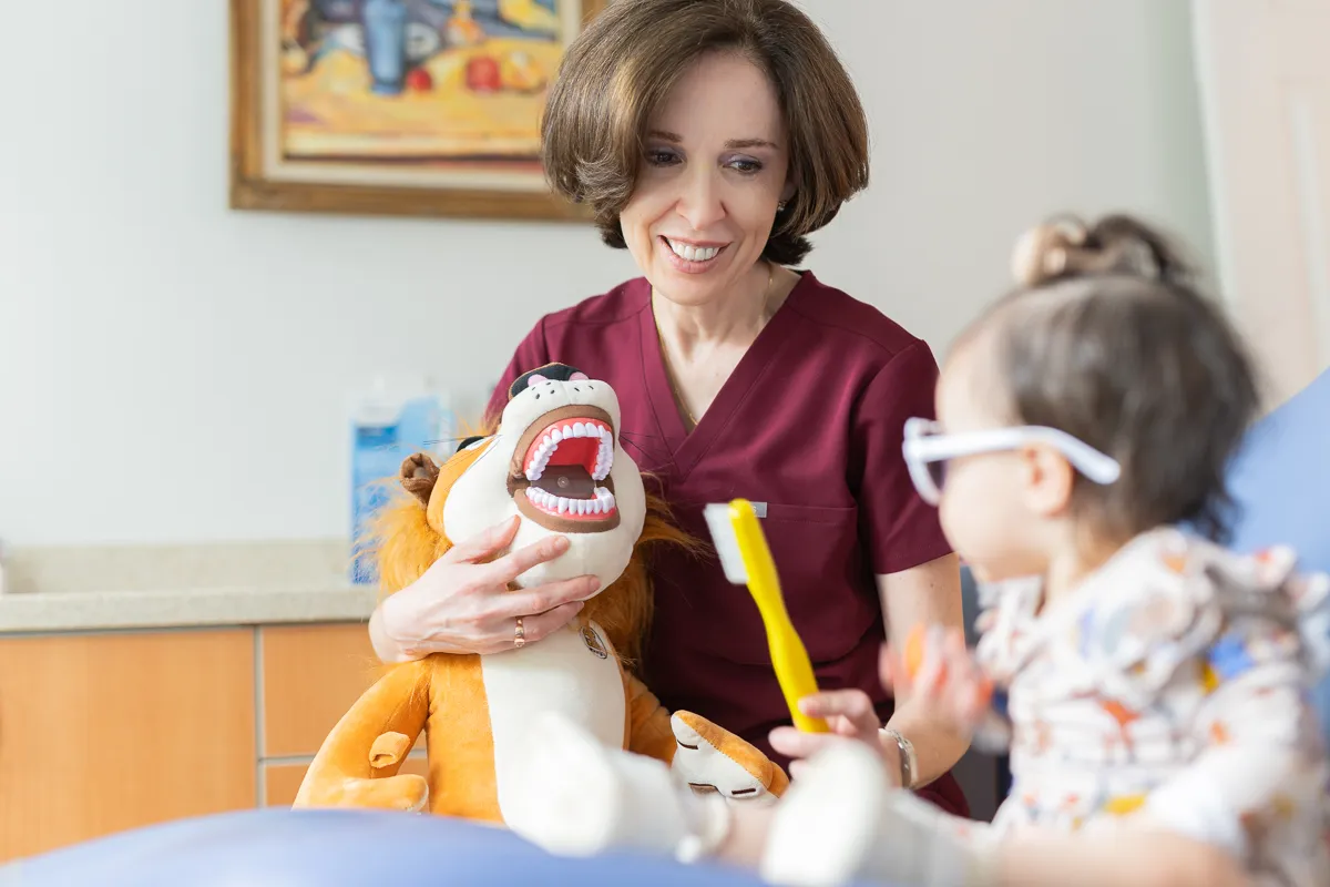 A dentist using a puppet to teach a young child about toothbrushing at Darien Pediatric Dentistry